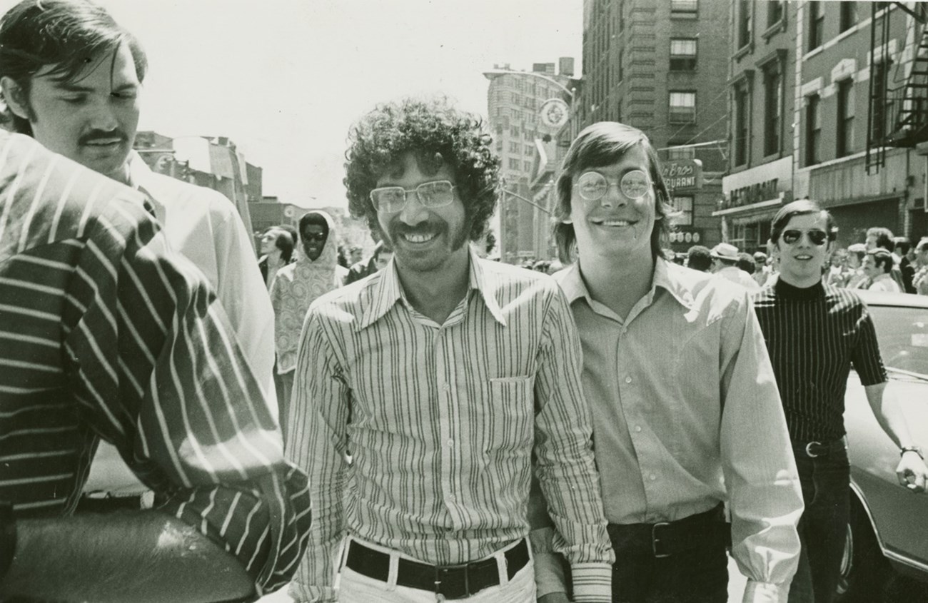 Two men holding hands and smiling while marching in the Christopher Street Liberation Day march on June 28, 1970